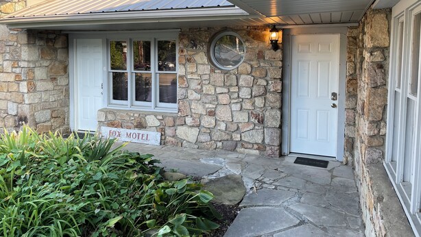A stone building with a sign reading "Fox Motel," a white door, and a window with a view of the street.