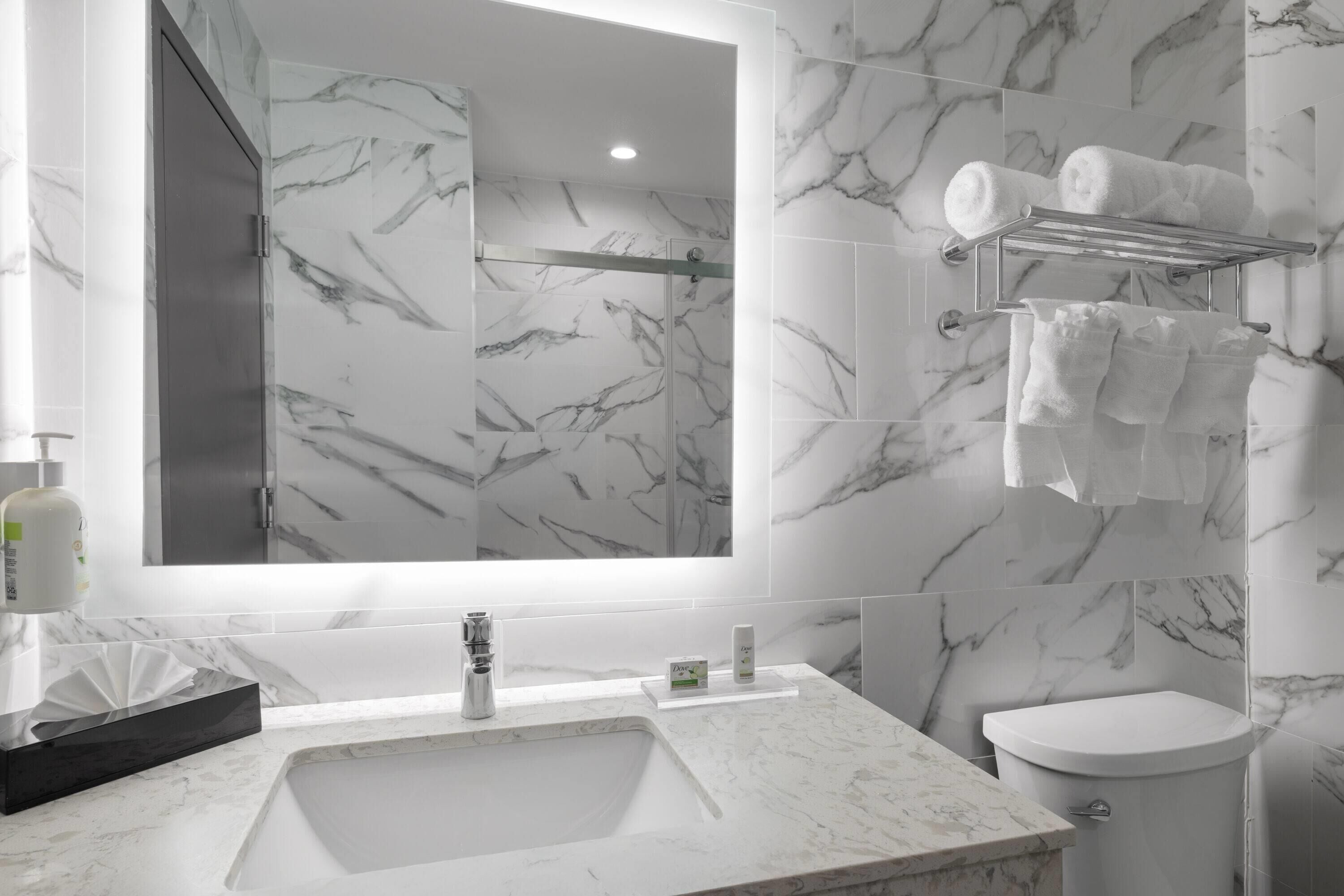 Un baño moderno con lavamanos de mármol, un inodoro y un perchero con toallas.