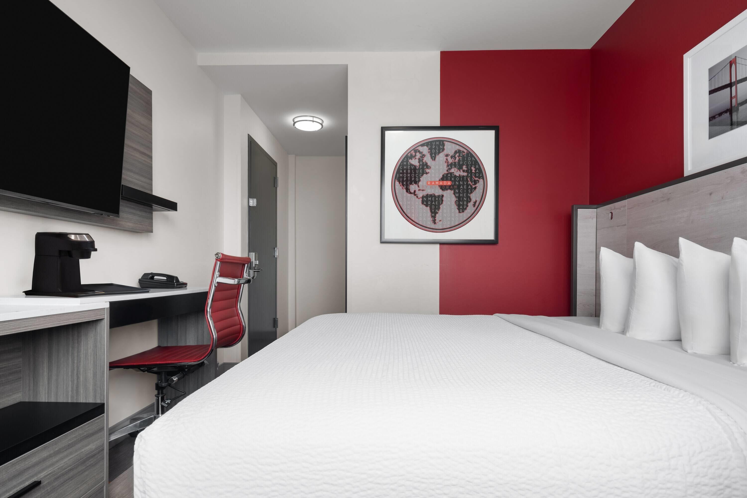 A hotel room with a bed, a desk with a chair, a coffee maker, and a framed world map on the wall.