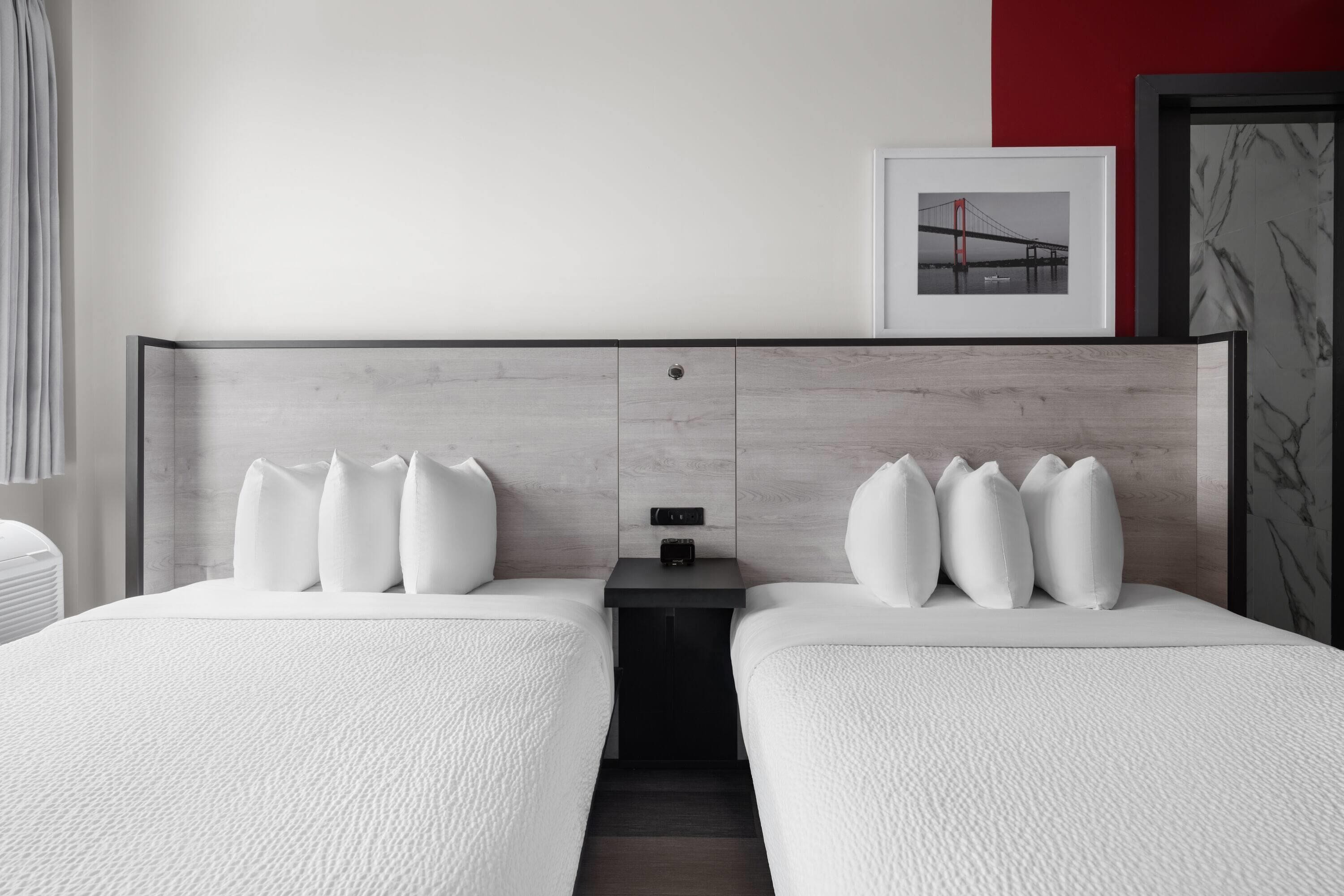 A hotel room with two beds, a nightstand, a framed picture, and a red accent wall.
