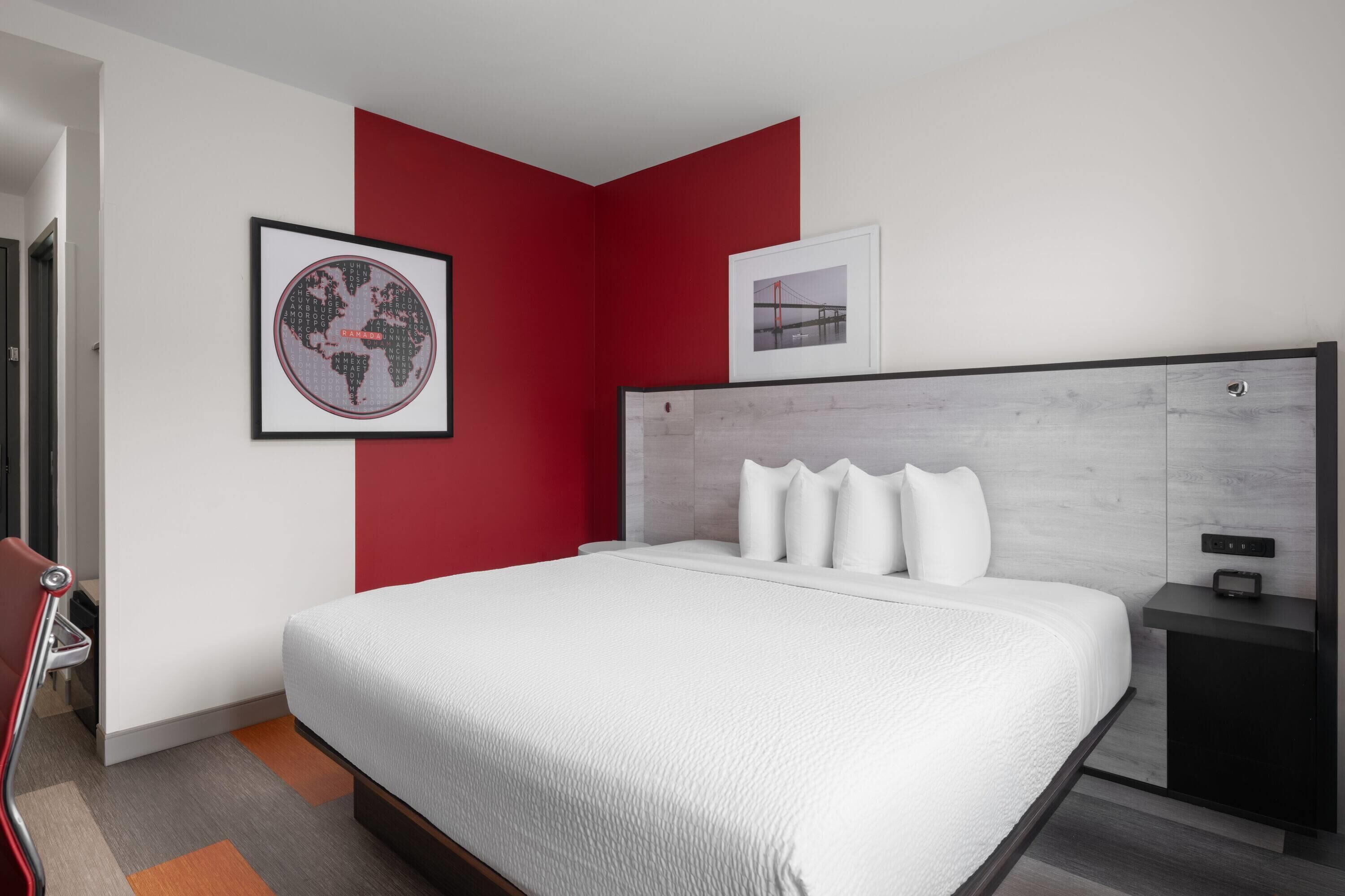 Una habitación de hotel moderna con una cama grande, una pared de acento roja y un mapa del mundo enmarcado.