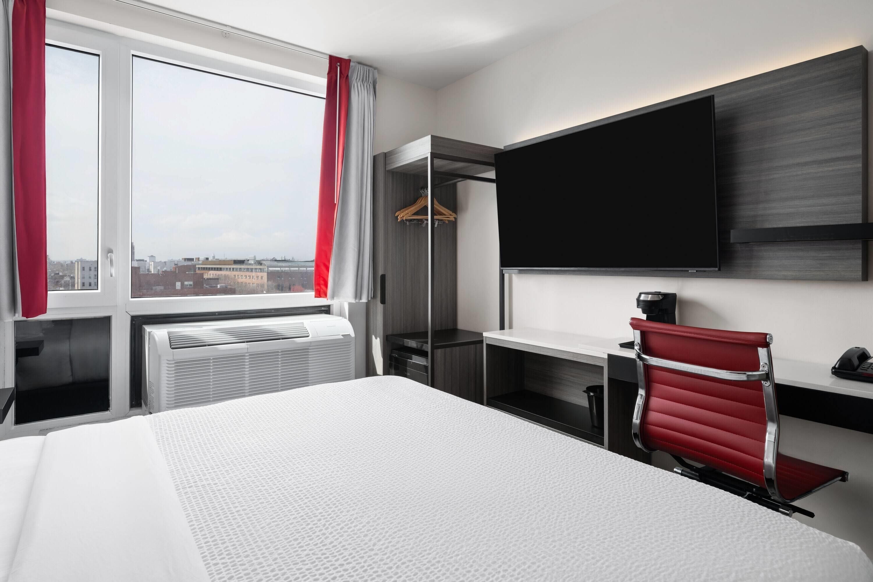 A hotel room with a bed, a desk, a chair, a TV, and a window with curtains.
