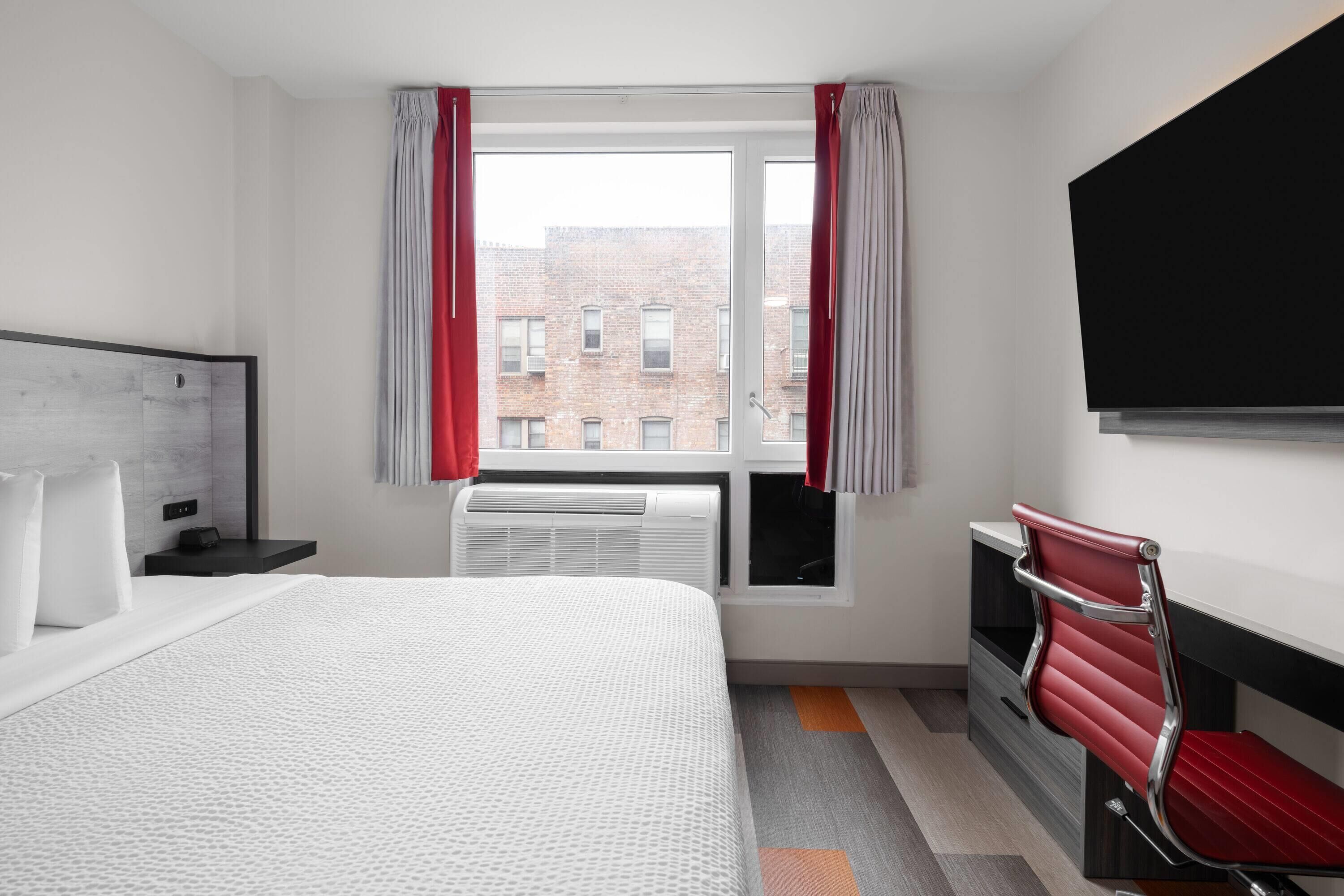 Une chambre d’hôtel avec un lit, un bureau, une chaise, une télévision et une fenêtre avec des rideaux.