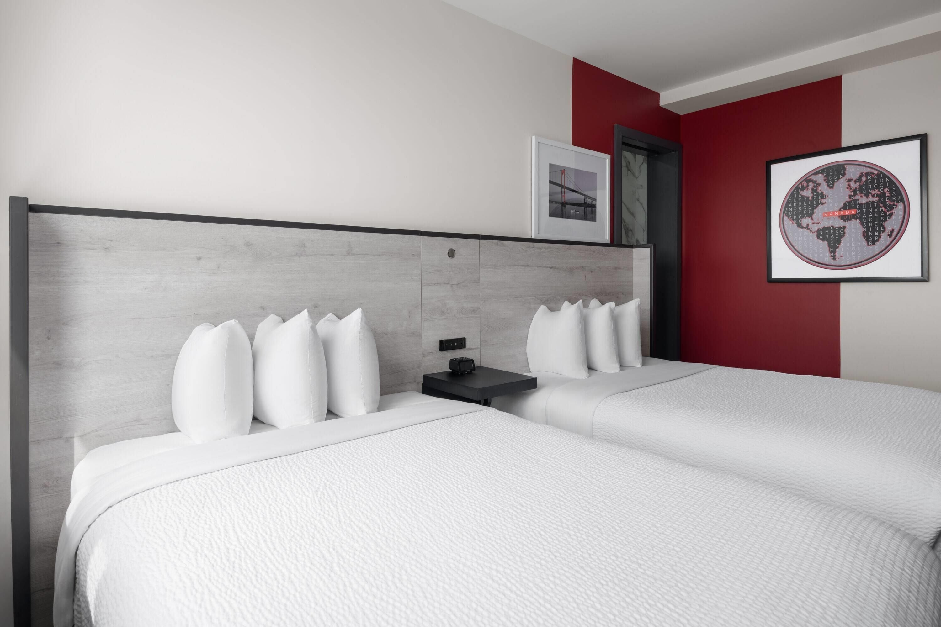 A modern hotel room with two beds, a nightstand, and a framed world map on the wall.