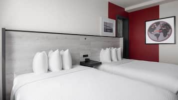 A modern hotel room with two beds, a nightstand, and a framed world map on the wall.