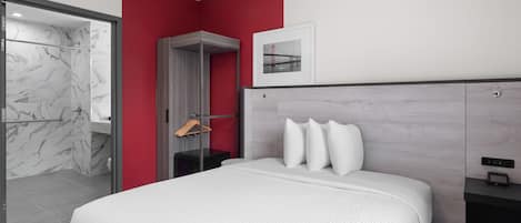 Een moderne hotelkamer met een bed, een rode accentmuur, een ingelijst kunstwerk en een douche.
