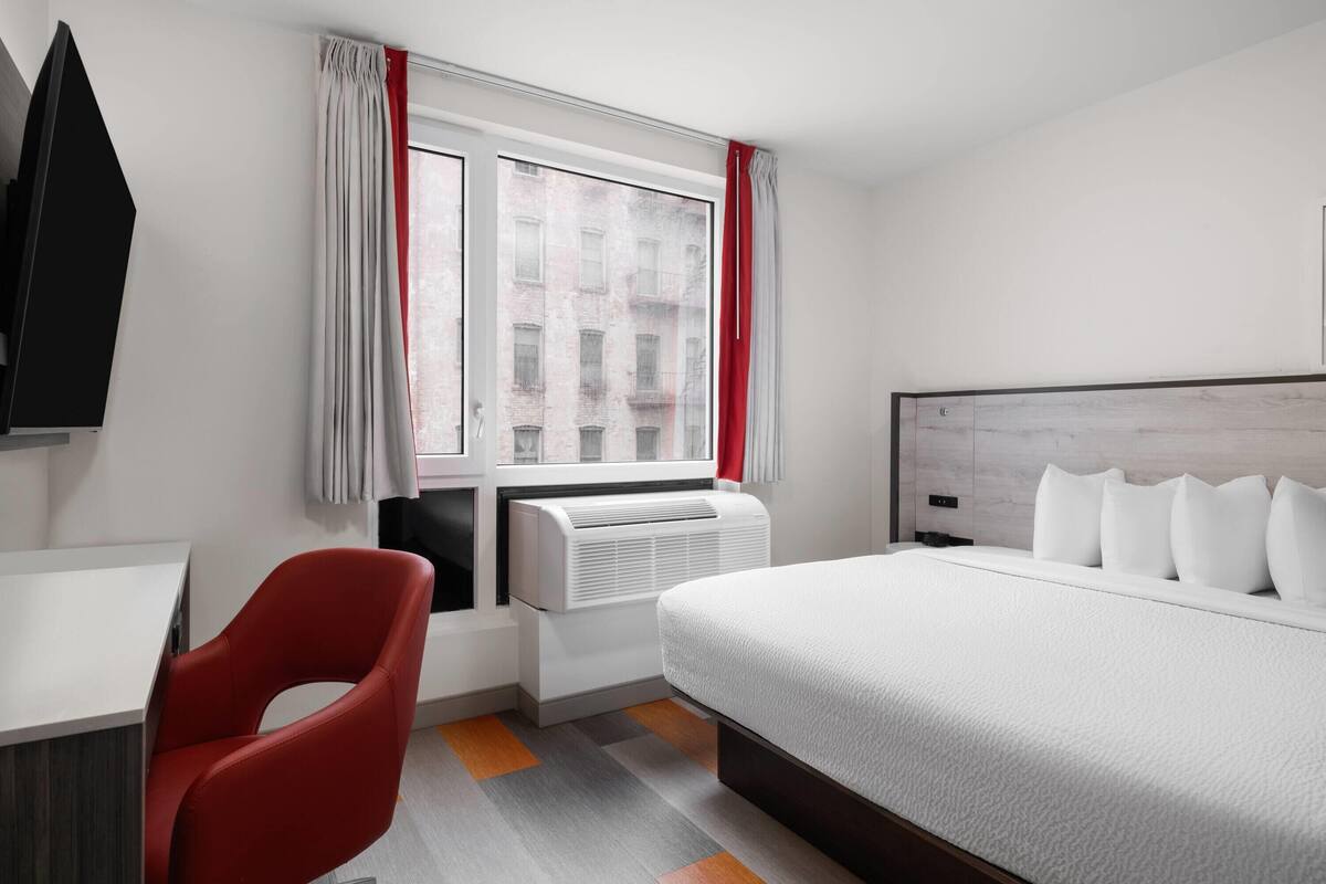 Ein Hotelzimmer mit Bett, Schreibtisch, Stuhl und einem fensterbepflanzten Fenster.
