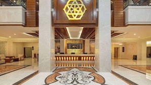 Een ruime lobby met een centraal receptiegedeelte, een geometrische lamp en een vloer met een patroon.
