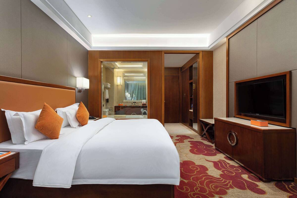 Ein Hotelzimmer mit einem großen Bett, einem Fernseher, einem Kleiderschrank und einem durch eine offene Tür einsehbaren Badezimmer.
