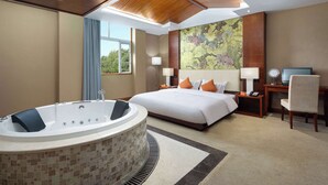 Een hotelkamer met een groot bed, een zithoek met een bureau en stoel, een groot raam en een bad.
