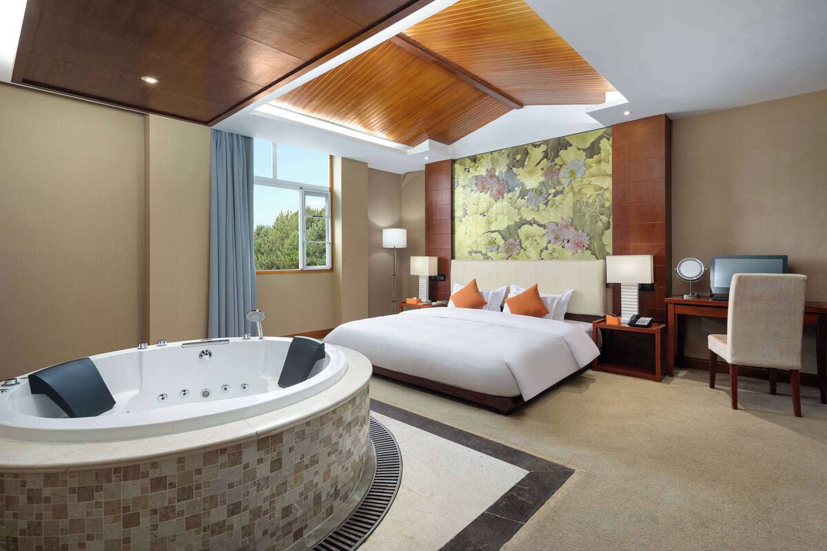 Ein Hotelzimmer mit einem großen Bett, einer Sitzecke mit Schreibtisch und Stuhl, einem großen Fenster und einer Badewanne.