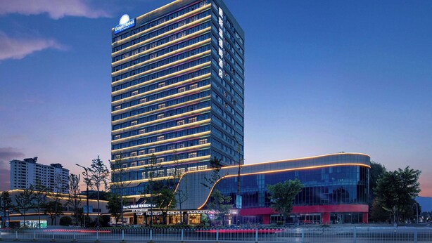 Un hôtel moderne, reconnaissable à son grand panneau « Days Hotel », avec de nombreux étages et une façade incurvée en verre.