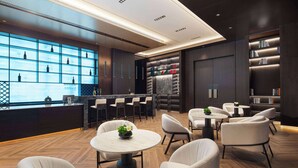 Un hall d’hôtel moderne avec un bar, des espaces aménagés pour s’asseoir et une grande fenêtre où sont exposées des bouteilles.