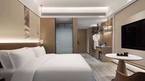 Une chambre d’hôtel moderne avec un grand lit, une petite table ronde, une télévision et une salle de bain équipée d’un miroir et d’un lavabo.