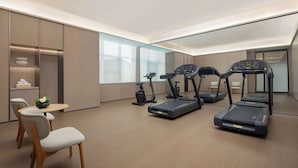 Une salle de sport moderne équipée de tapis de course, de vélos d’appartement et d’un petit coin repas avec des chaises et une table.