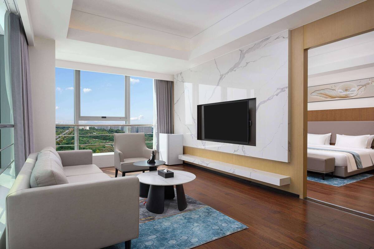 A modern hotel room with a large TV, a sofa, a coffee table, and a bed.