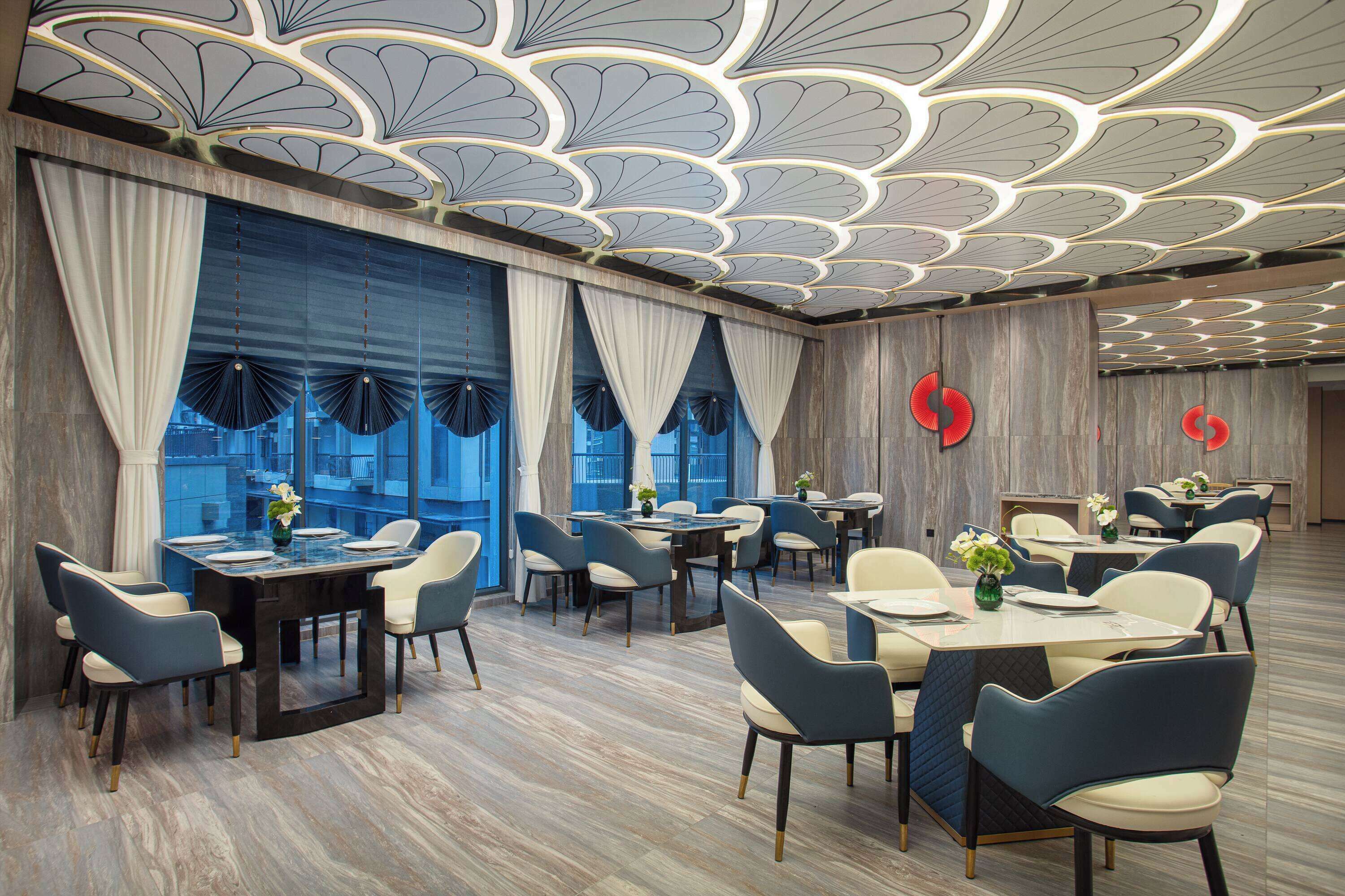 Un espace de restauration moderne, avec des tables et des chaises, de grandes fenêtres agrémentées de rideaux et un plafond décoratif.