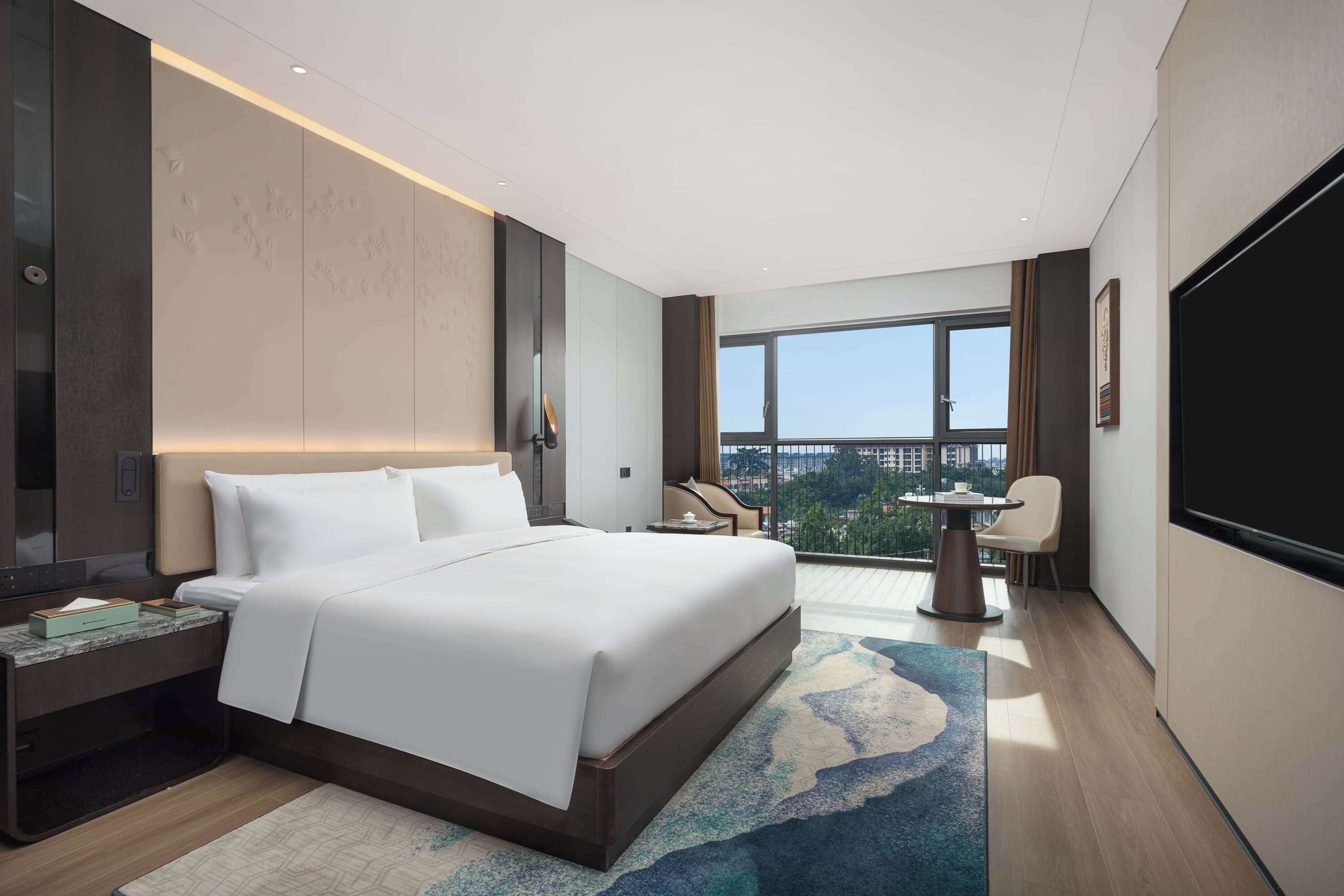 Een moderne hotelkamer met een groot bed, een bureau, een stoel, een televisie en een balkon met uitzicht op de stad.