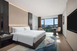 Une chambre d’hôtel moderne dotée d’un grand lit, d’un bureau, d’une chaise, d’une télévision et d’un balcon offrant une vue sur la ville.
