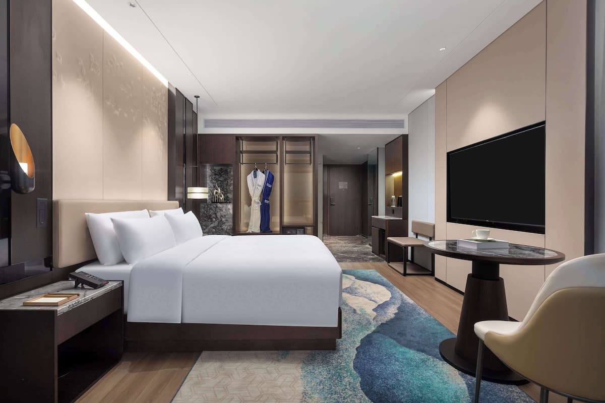 Ein modernes Hotelzimmer mit einem großen Bett, einem Fernseher, einem Schreibtisch und einer Sitzecke.