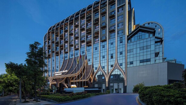 Un hotel moderno con una fachada curva distintiva, varios balcones y una entrada destacada con señalización iluminada.