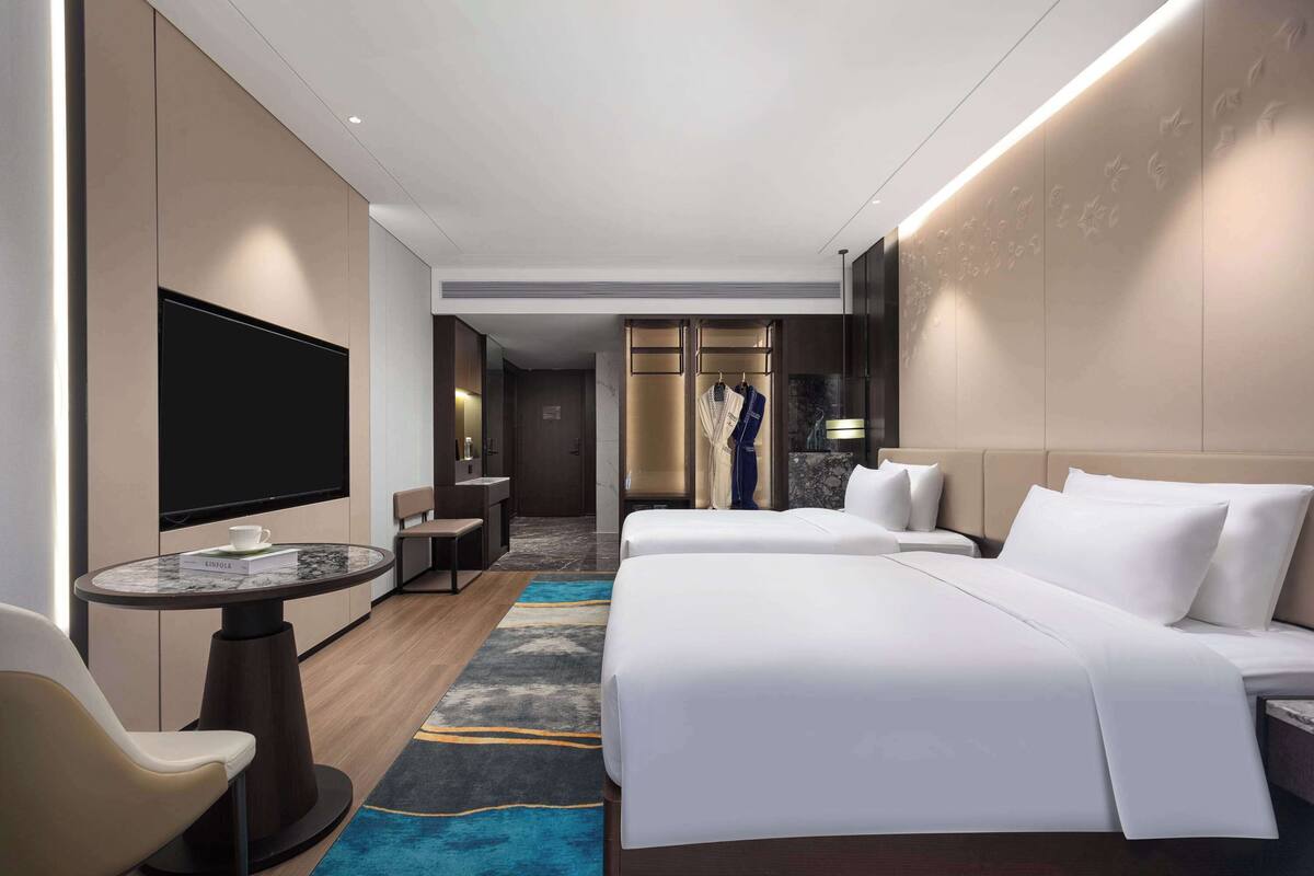 Ein modernes Hotelzimmer mit einem großen Bett, einem Fernseher, einer Sitzecke und einem Kleiderschrank.