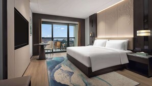 Un hotel moderno con una cama grande, un escritorio, una silla y vistas de la ciudad a través de amplias ventanas.