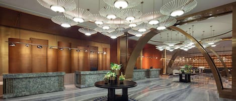 A lobby with a marble floor, a reception desk, and a round table with plants.
