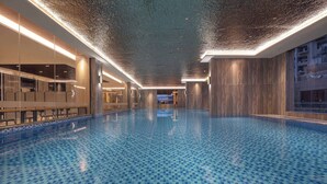 Una amplia piscina interior con suelo de baldosas azules formando un diseño de tablero de ajedrez, rodeada de paredes con superficie reflectante y un techo con textura.