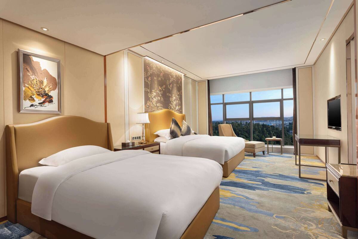 Quarto de hotel com duas camas, televisão, escrivaninha e vista para a cidade.