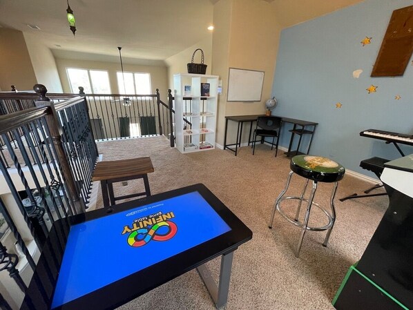 Una habitación amplia con alfombra azul, una pantalla digital que muestra 'INTERNATIONAL', una pizarra y un piano.