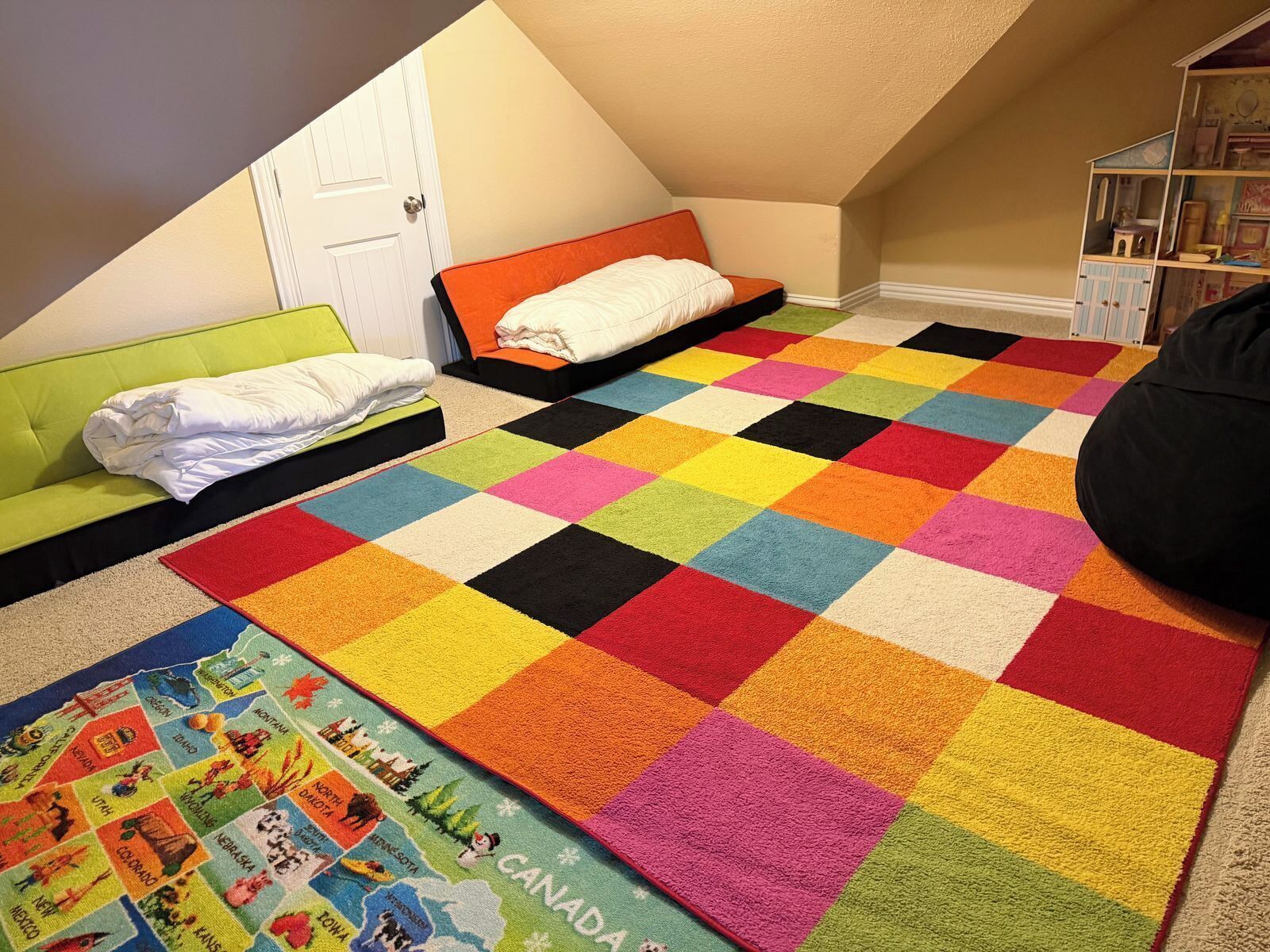 Una habitación con techo inclinado, dos camas con ropa de cama colorida, una alfombra multicolora y una pequeña estantería.
