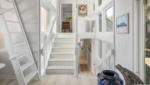 Un escalier menant au deuxième étage, avec des rampes blanches et une vue sur la cuisine située en contrebas.