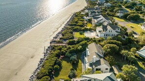 Vue aérienne d’une zone résidentielle côtière, avec des maisons le long de la plage, un ciel dégagé et une mer calme.