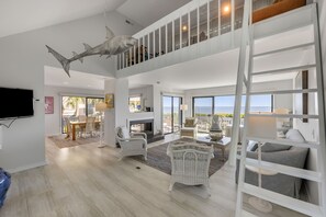 A spacious living area with a high ceiling, a large fish mural, a balcony with a view, and a TV mounted on the wall. -  Oceanfront, vintage beach house steps from the sand on Seabrook Island. (Johns Island)