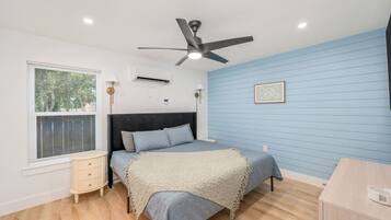 A bedroom with a bed, a ceiling fan, a window with blinds, a bedside table, and a nightstand.