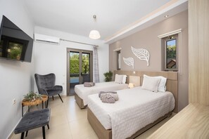 Un dormitorio con dos camas, televisor, una silla, una mesita y ventana con vistas.