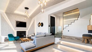 A modern living room with a sofa, a teal armchair, a fireplace, and a staircase. - Villa Vatia 3 - Three Bedroom Villa, Sleeps 8 (Ionian Islands)