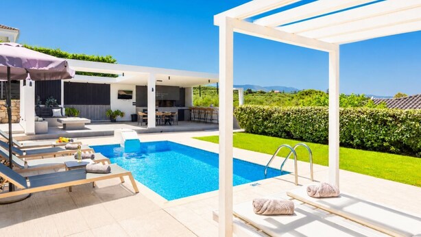 Uma área de piscina moderna ao ar livre com espreguiçadeiras, um espaço de estar coberto e vista para a paisagem.