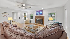 A spacious living room with a fireplace, leather sofas, a coffee table, and a ceiling fan.