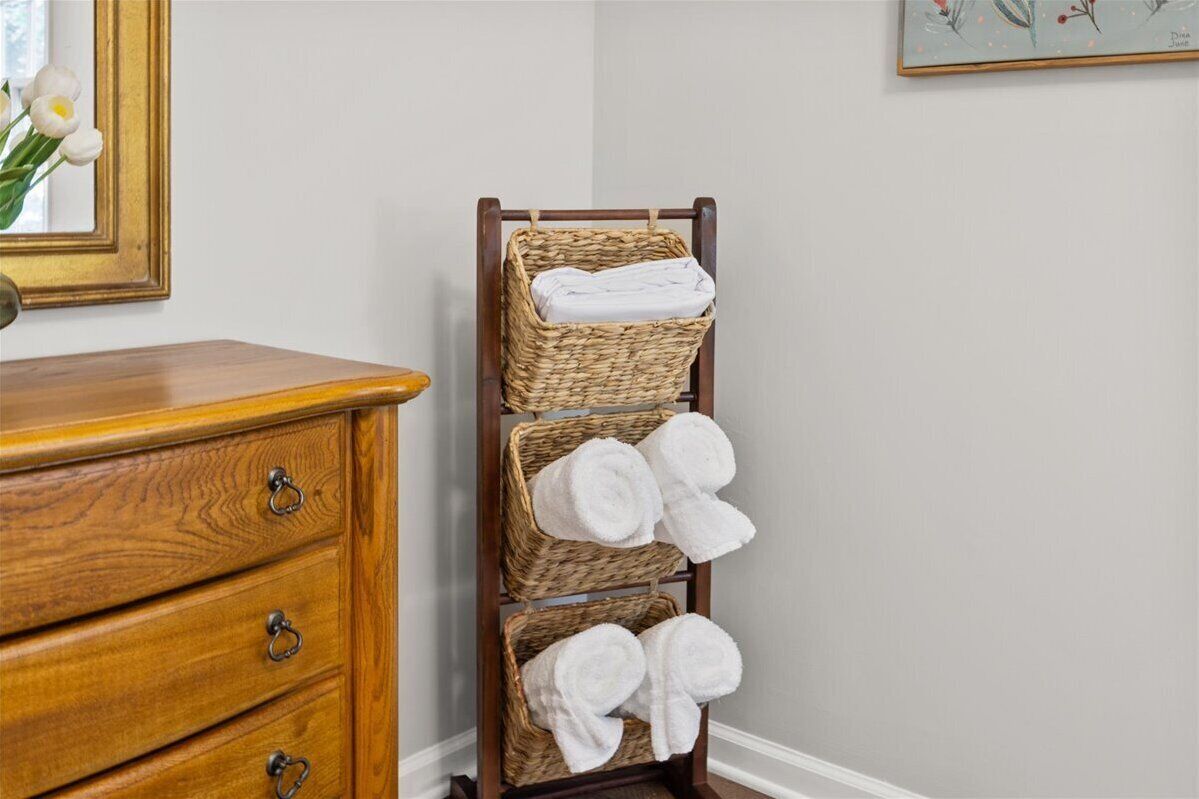A wooden dresser with three drawers and a tall wicker towel rack with towels.