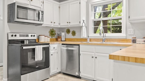 A modern kitchen with white cabinetry, stainless steel appliances, and a wooden countertop.