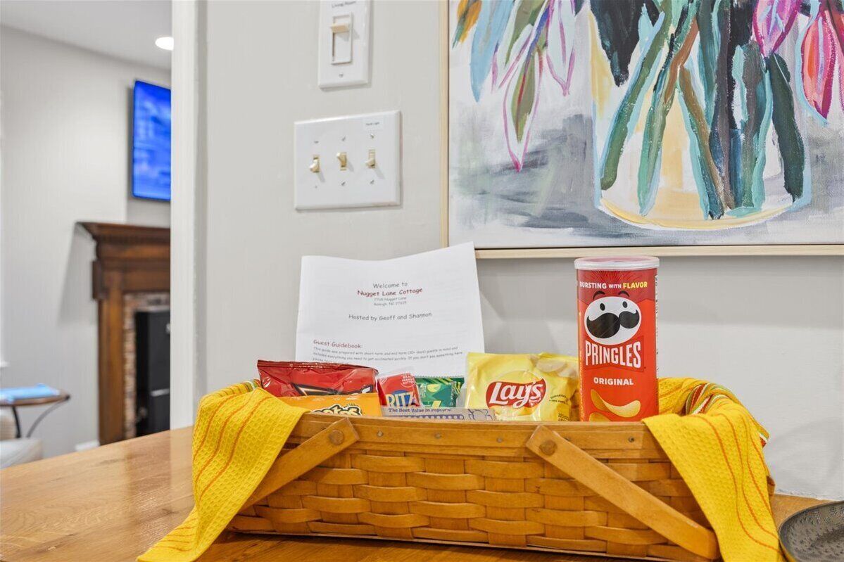 Un cesto con snack e una guida per gli ospiti su un tavolo in una stanza con un quadro appeso al muro.