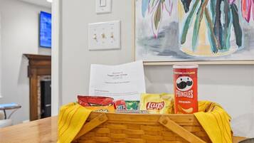 Un cesto con snack e una guida per gli ospiti su un tavolo in una stanza con un quadro appeso al muro.