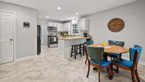 A modern kitchen with white cabinets, a central island, and a dining area with a wooden table and blue chairs.