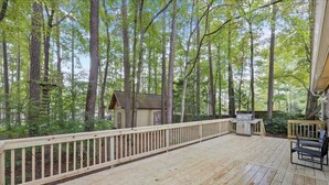 A wooden deck with a grill and seating area, surrounded by tall trees.