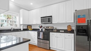 Una cocina moderna con armarios blancos, electrodomésticos de acero inoxidable y encimera negra.