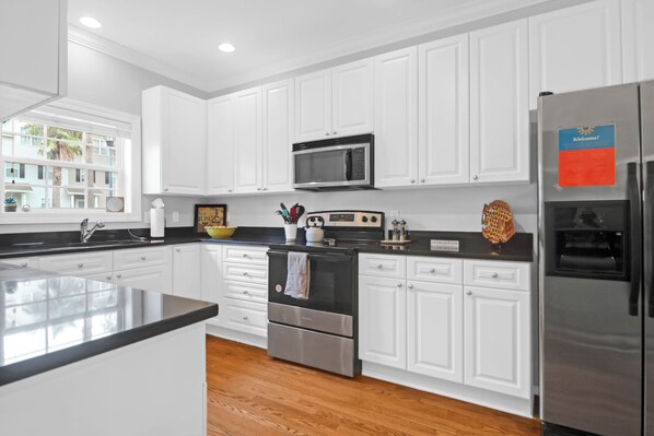 A modern kitchen with white cabinets, stainless steel appliances, and a black countertop.