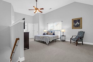 A bedroom with a bed, bedside lamps, a chair, a ceiling fan, and a framed picture on the wall.