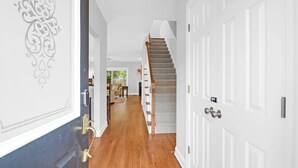 Un pasillo con suelo de madera, paredes blancas y una escalera que lleva a una distribución.